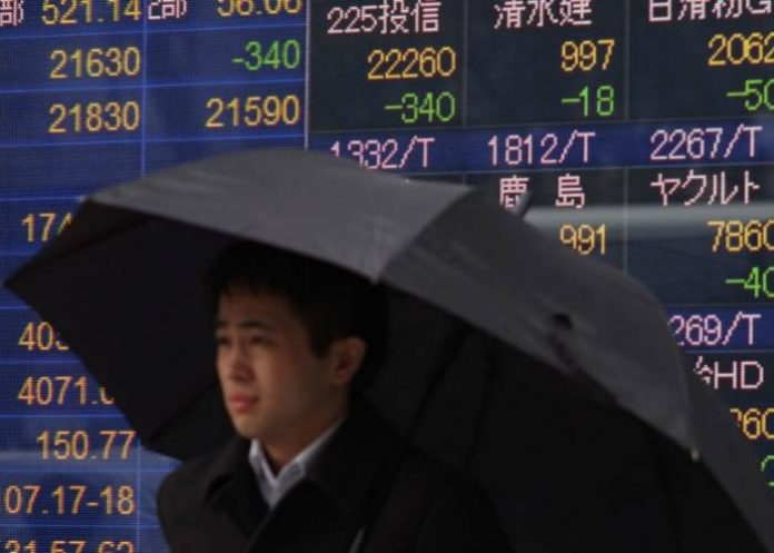 A pedestrian stands in front of an electronics stock indicator displaying individual stock prices on the Tokyo Stock Exchange in Tokyo on February 22, 2018. Tokyo stocks opened lower on February 22 following falls on Wall Street after minutes from the US central bank's last meeting solidified expectations of interest rate hikes ahead. / AFP PHOTO / Kazuhiro NOGI